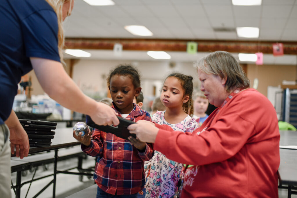 Stem educator and school teacher help two young students get set up with a robot ball.