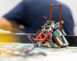 A LEGO robot sits on a table with a person in the background.
