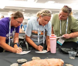 Three individuals are focused on signing papers at a table with rocks.