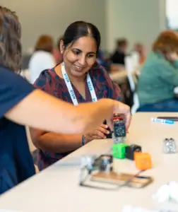 Two individuals collaborate on a STEM project at a table, with one smiling as they work together with small robotic components.