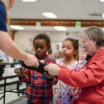 Stem educator and school teacher help two young students get set up with a robot ball.