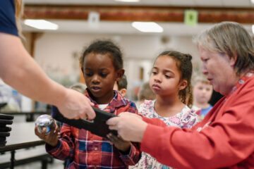 Stem educator and school teacher help two young students get set up with a robot ball.